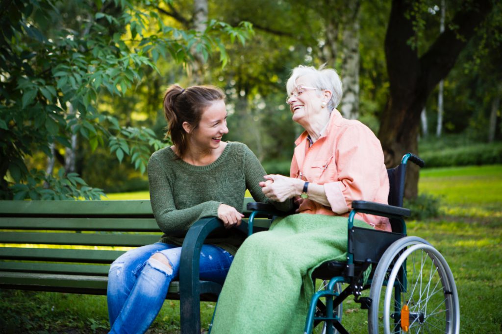 Senior woman in wheelchair enjoying time in the park with caregiver