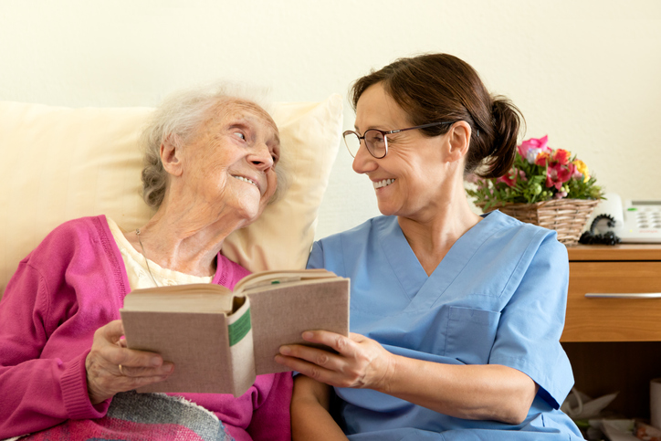 Female nurse with senior woman patient, reading a book