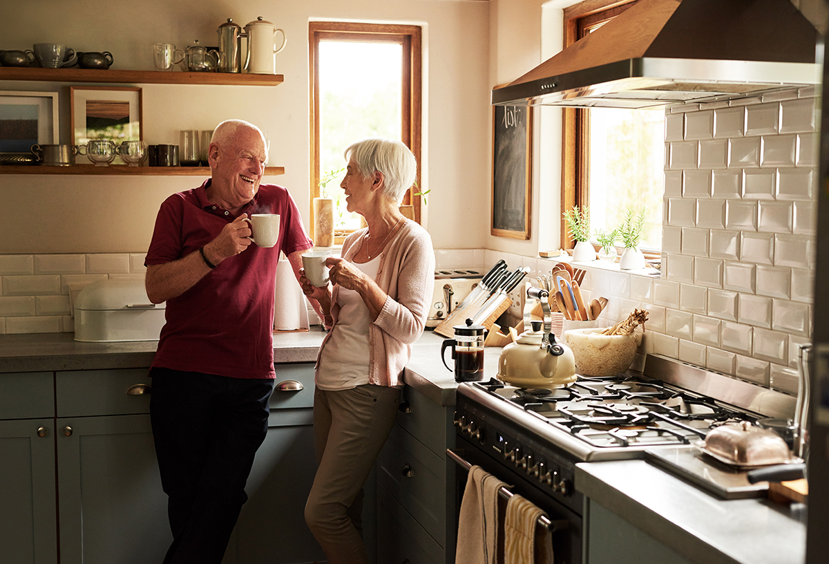 Older couple enjoys coffee together in their kitchen and discuss at home dementia care safety.