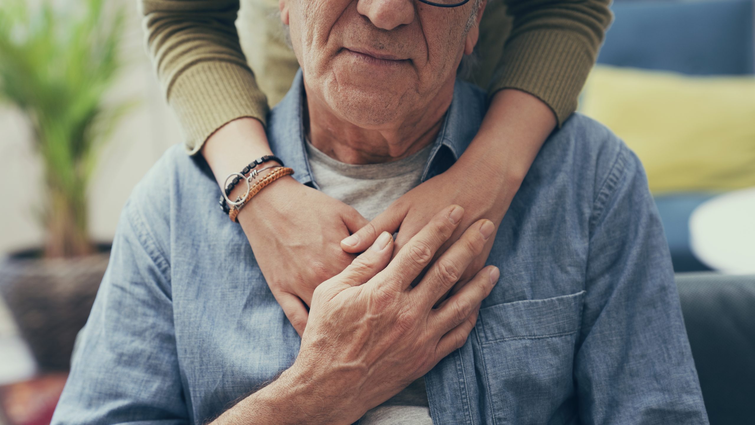 Senior man rested in a seated position while receiving an embrace from behind