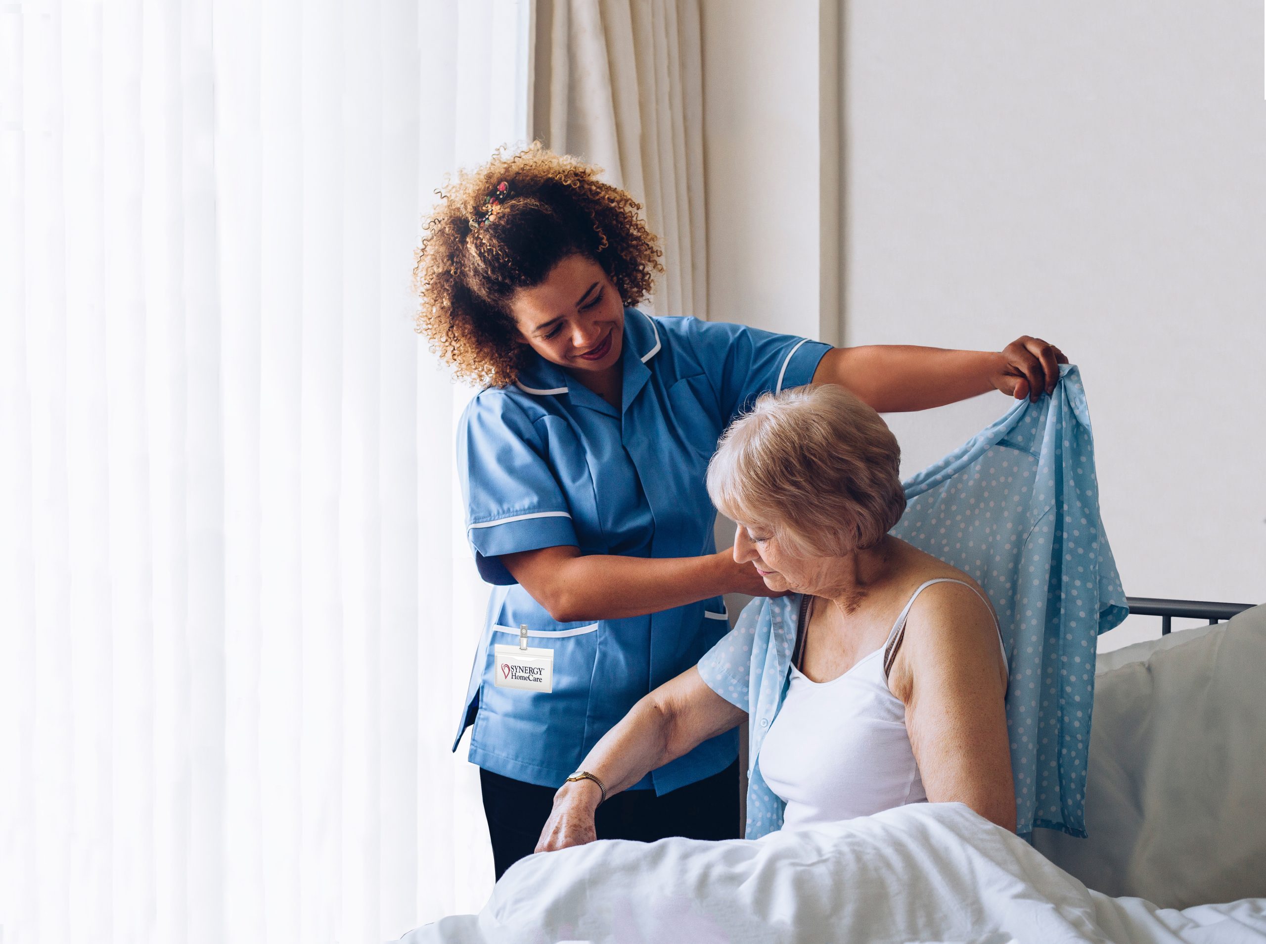 SYNERGY HomeCare caregiver helping client put clothes on.