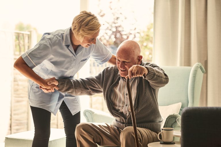 Female healthcare worker supporting senior man at care home