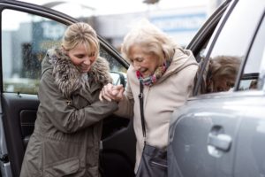 Woman helping senior woman out of car