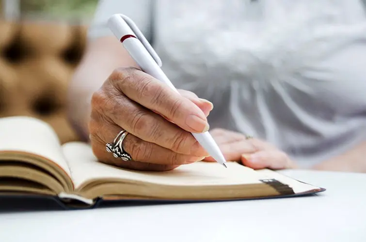 senior hand with pen writing in journal