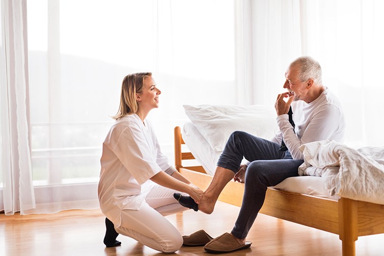 female caregiver helping senior man out of bed