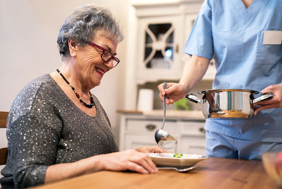caregiver laddling soup into a bowl for senior woman