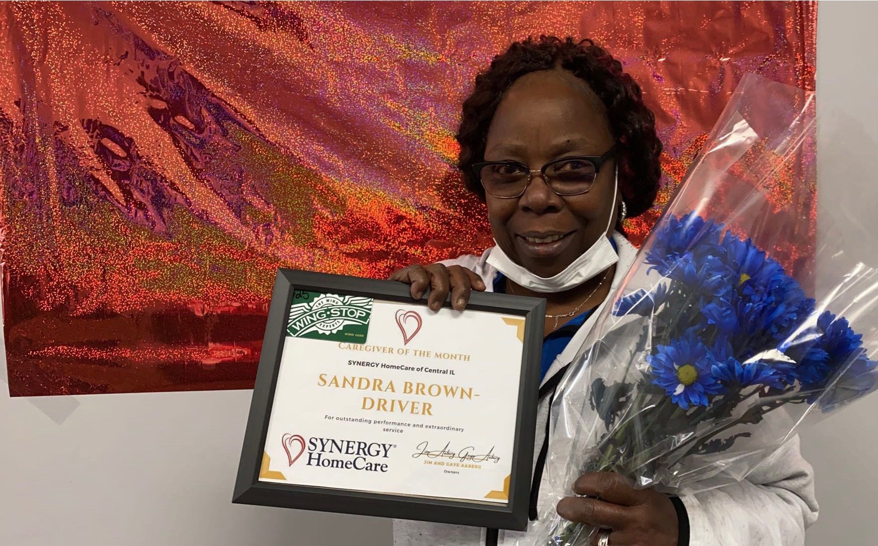 caregiver of the month sandra brown smiles while holding her award and flowers that she got for being the best home care caregiver
