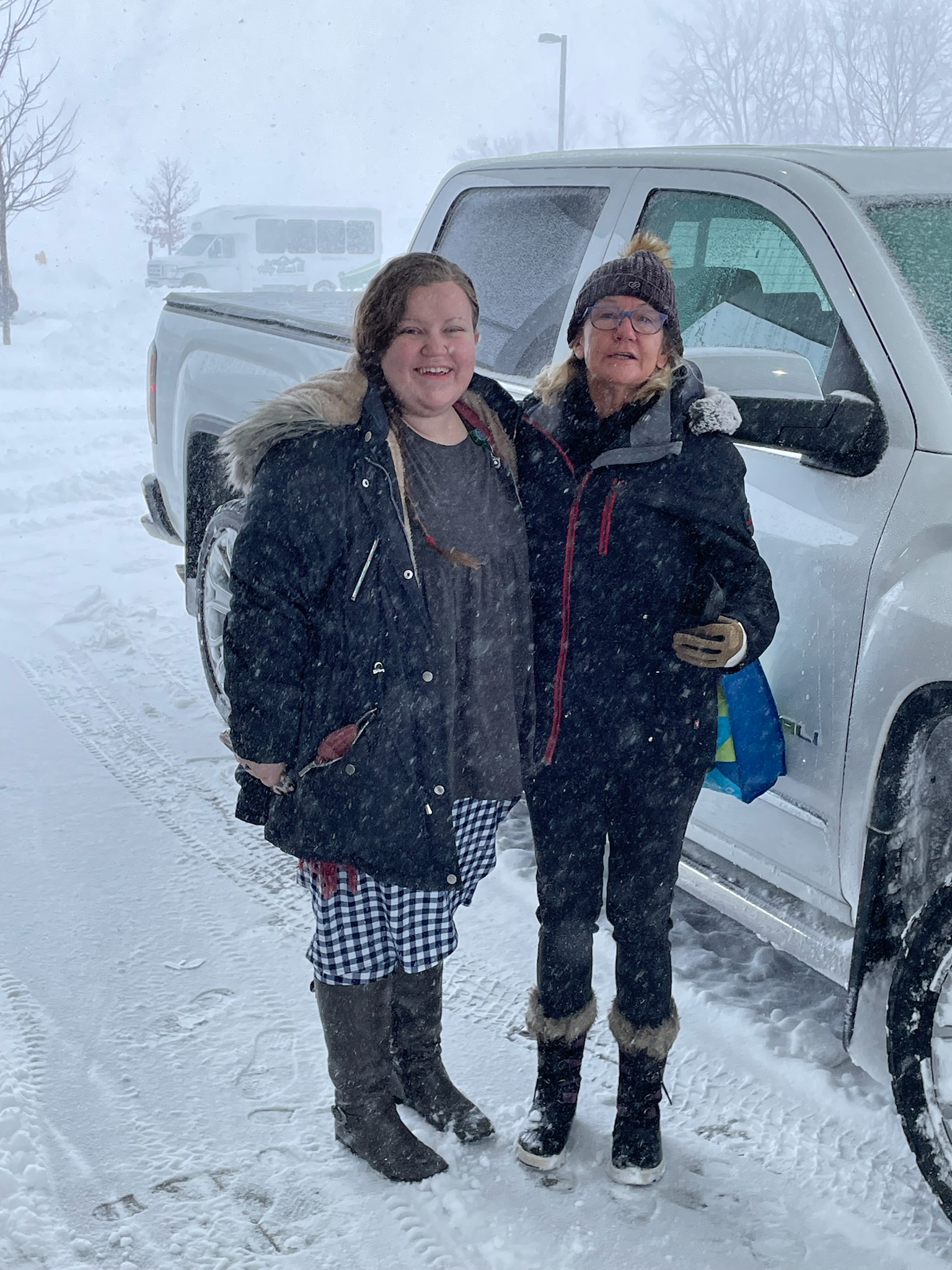 Caregiver and SYNERG HomeCare of Central IL owner Gaye aaberg pose by a pickup truck bundled in snow gear in a snowstorm