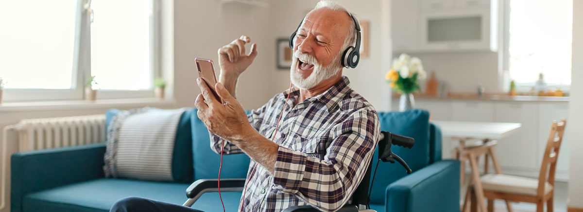 senior man in wheelchair enjoying listening to music as he looks at his smartphone